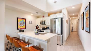 A modern kitchen with a central island, bar stools, stainless steel appliances, and a hallway with patterned wallpaper.