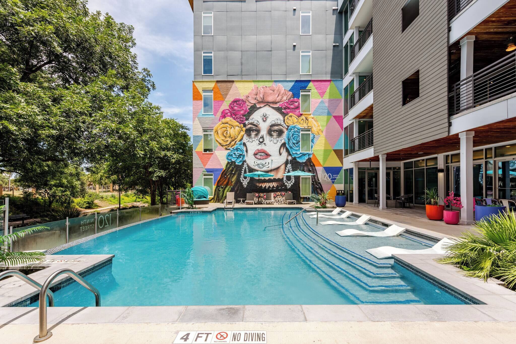 A swimming pool with a mural, a 4 ft no diving sign, and a building with balconies.