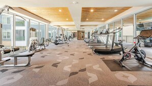 Une salle de sport équipée de divers appareils d’exercice, dotée de grandes fenêtres et d’un plafond en bois.