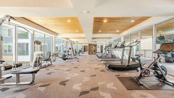 A gym with various exercise equipment, large windows, and a wooden ceiling.