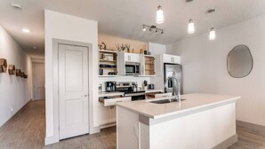 Une cuisine moderne avec des meubles blancs, un îlot central doté d’un évier et des luminaires suspendus.
