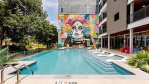 Une piscine ornée d’une fresque murale, un panneau indiquant une profondeur minimale de 1,20 mètre pour la plongée, et un bâtiment doté de balcons.