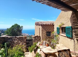 A stone building with a view of the sea, a small window with shutters, and potted plants. - A beautiful elevated architect designed villa with breathtaking sea views. (Costa Paradiso)