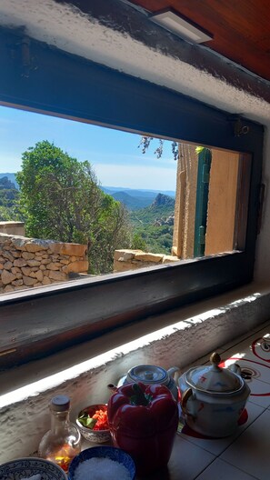 A window view of a mountainous landscape, a stone wall, and a table with kitchen items. - A beautiful elevated architect designed villa with breathtaking sea views. (Costa Paradiso)