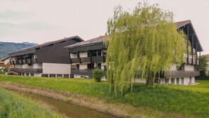 En moderne bygning med flere balkoner, en flod i forgrunden og et træ til højre.