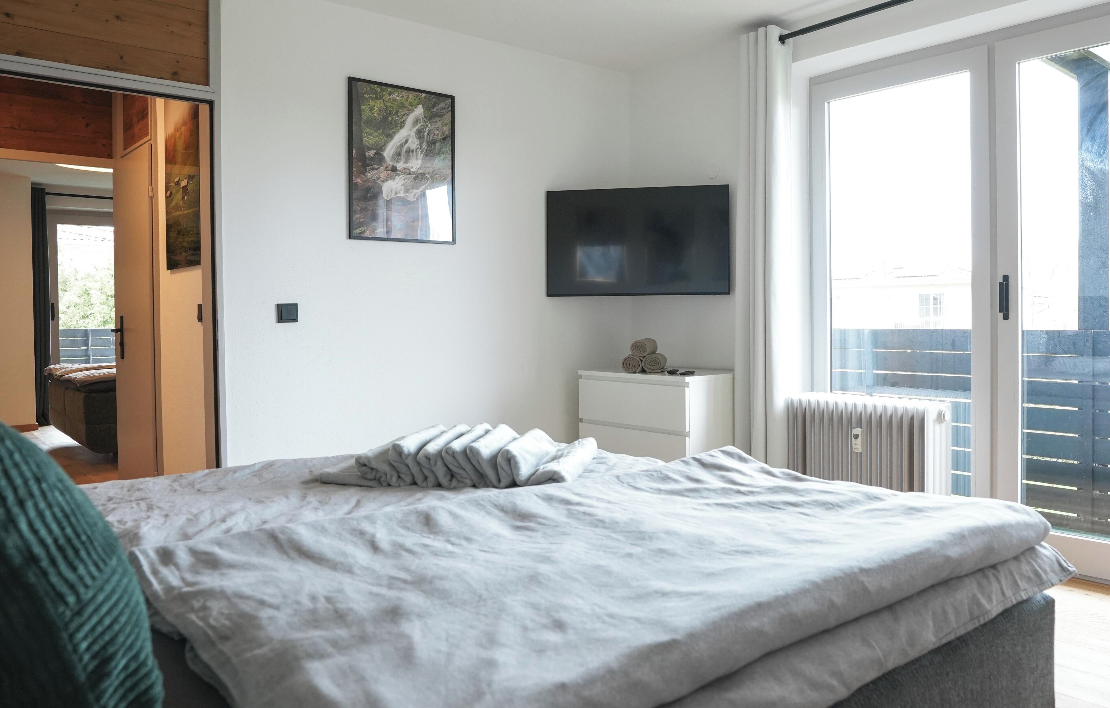 Una camera da letto con un letto, una televisione, una finestra vista e una porta che conduce a un'altra stanza.