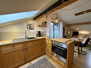 A modern kitchen with wooden cabinets, a built-in oven, and a skylight. - Slice wall loft vacation apartment 55 sqm, open living room and bedroom with balcony (Aschau im Chiemgau)