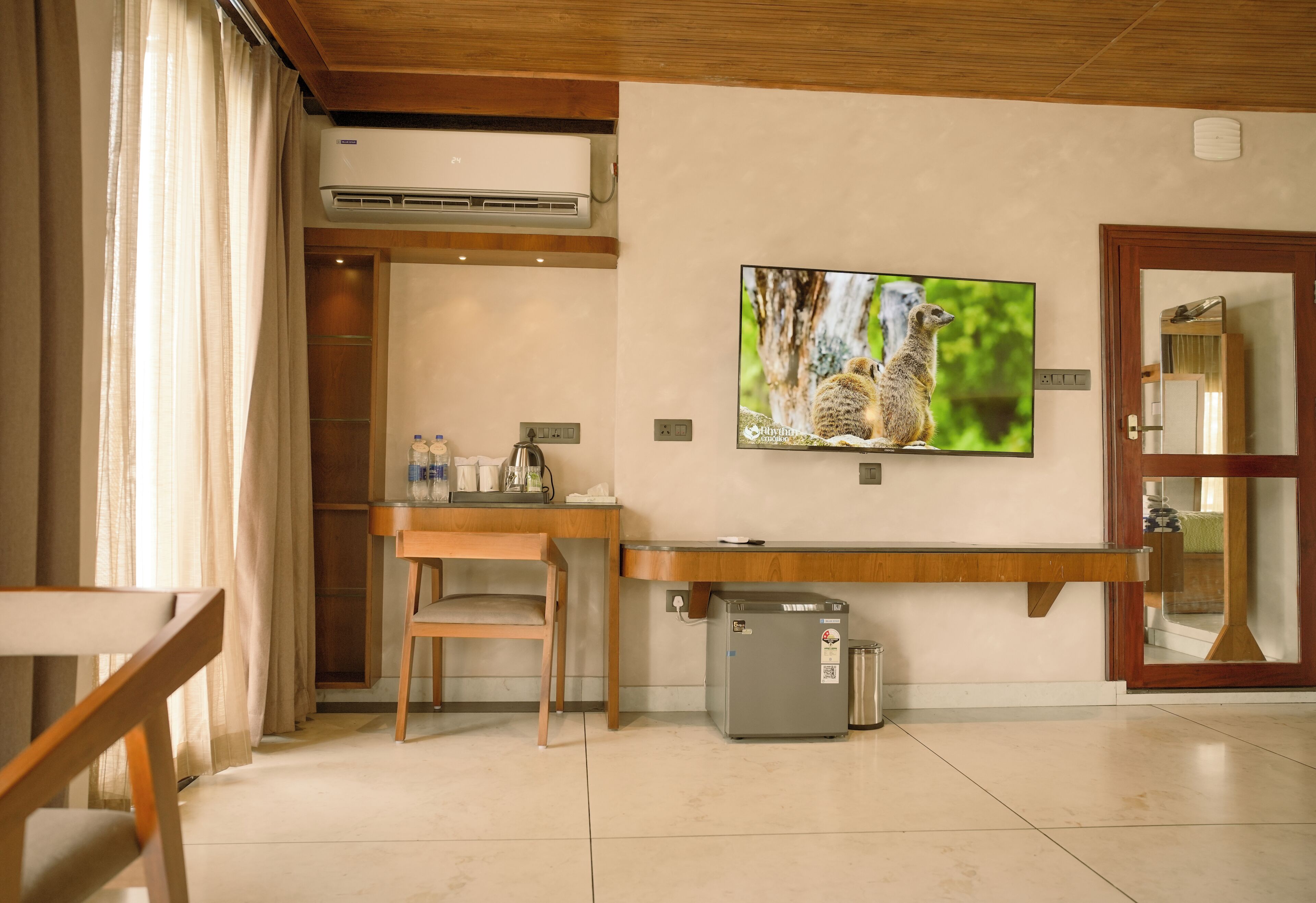 A room with a wooden desk, chair, air conditioning unit, TV, and a small refrigerator.