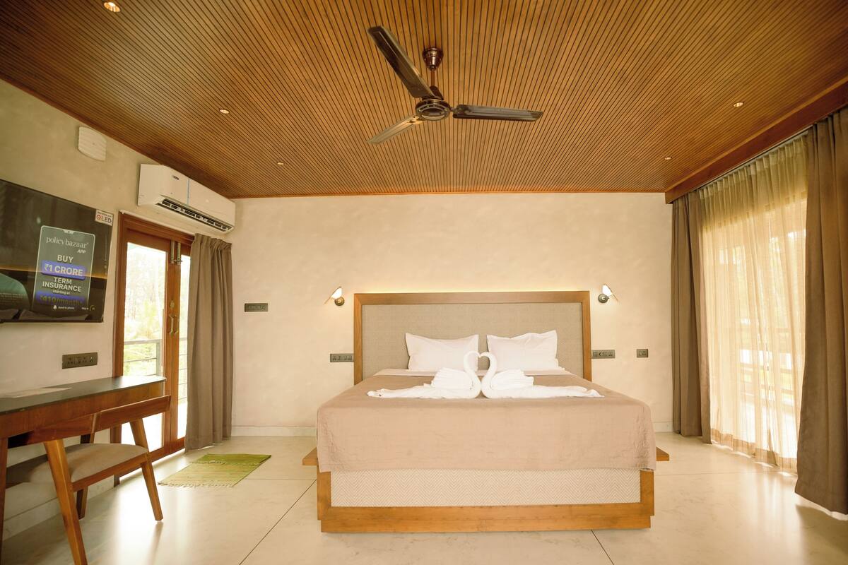 Habitación de hotel con techo de madera, una cama con dos almohadas, un escritorio y un televisor en la pared.