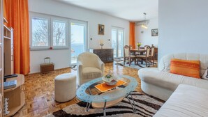 A spacious living room with a glass coffee table, a white sofa, and a dining area with a chandelier. - Vacation apartment with swimming pool, barbecue and sea view (Dramalj)