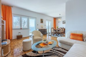 A spacious living room with a glass coffee table, a white sofa, and a dining area with a chandelier. - Vacation apartment with swimming pool, barbecue and sea view (Dramalj)