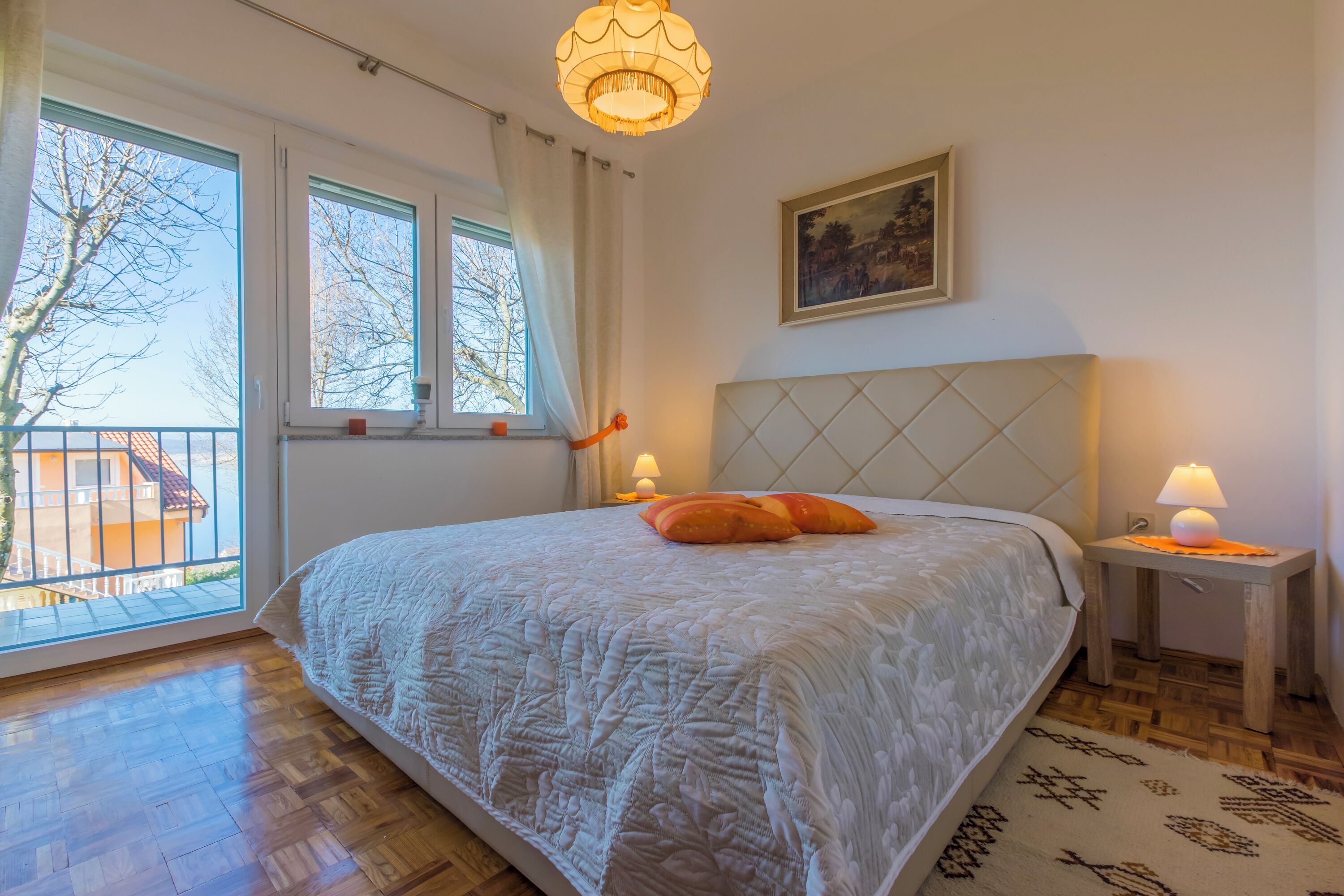 Une chambre à coucher avec un lit, une table de chevet, une lampe, une fenêtre avec des rideaux et un tableau au mur.