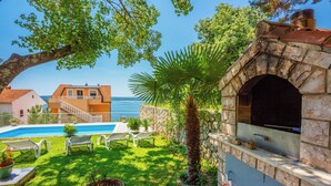 A pool with lounge chairs, a stone oven, and a view of the sea. - Vacation apartment with swimming pool, barbecue and sea view (Dramalj)