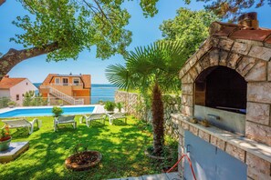 A pool with lounge chairs, a stone oven, and a view of the sea. - Vacation apartment with swimming pool, barbecue and sea view (Dramalj)