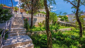 A residential area with stone steps leading to a balcony, surrounded by lush greenery and trees. - Vacation apartment with swimming pool, barbecue and sea view (Dramalj)