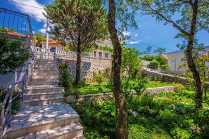 A residential area with stone steps leading to a balcony, surrounded by lush greenery and trees. - Vacation apartment with swimming pool, barbecue and sea view (Dramalj)