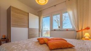 A bedroom with a large bed, a window with curtains, a bedside lamp, and a small table with a lamp. - Vacation apartment with swimming pool, barbecue and sea view (Dramalj)
