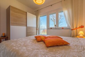 A bedroom with a large bed, a window with curtains, a bedside lamp, and a small table with a lamp. - Vacation apartment with swimming pool, barbecue and sea view (Dramalj)