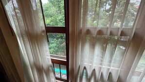 Een kamer met een groot raam, een houten trap en uitzicht op groen.