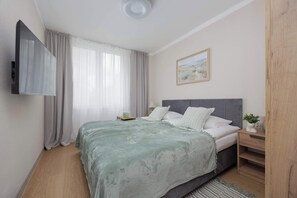 A bedroom with a bed, a bedside table, a lamp, a painting on the wall, and a window with curtains. - Comfortable Apartment | Two Bedrooms (Warszawa)