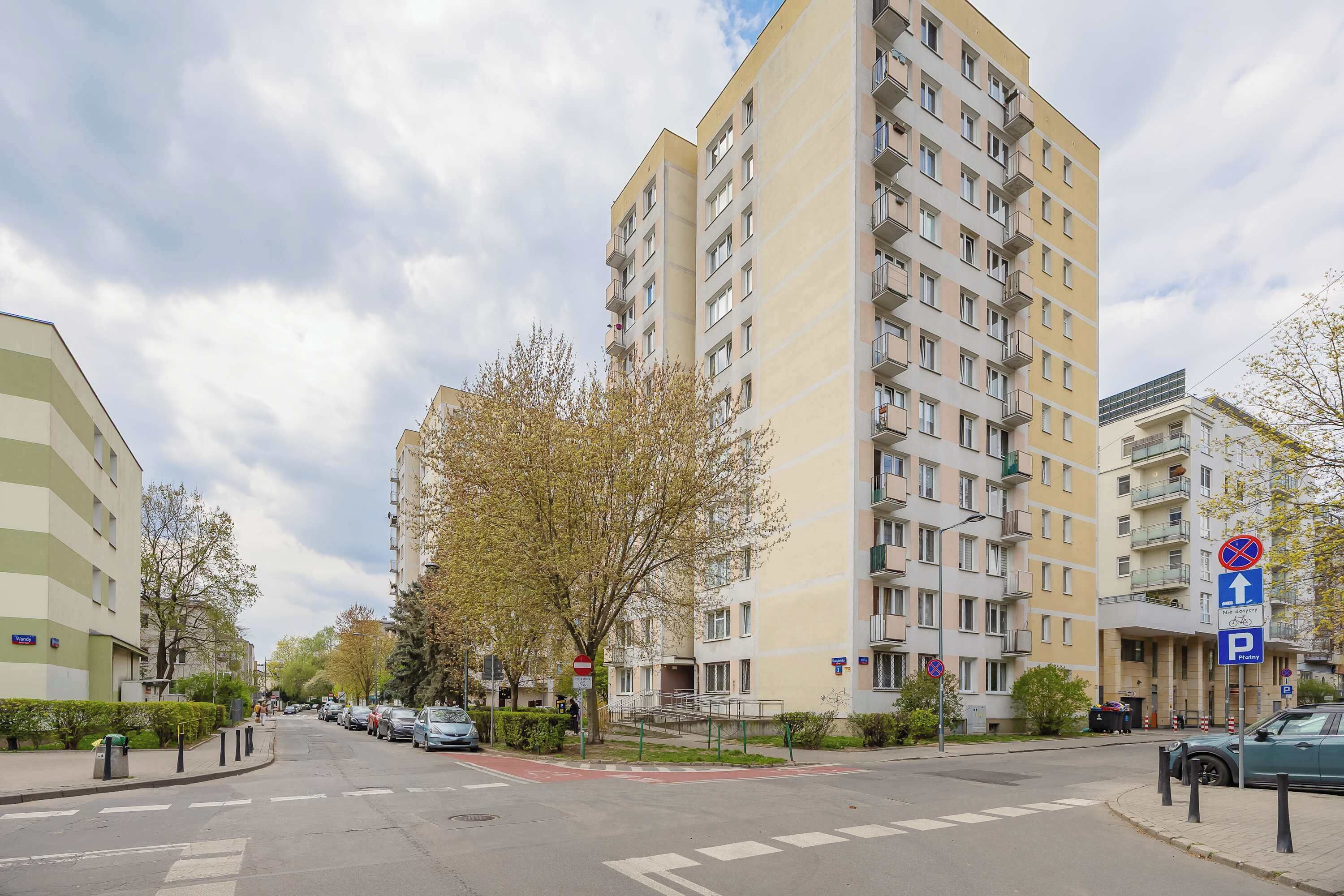 A multi-story residential building with balconies, a pedestrian crossing, and a parking sign.