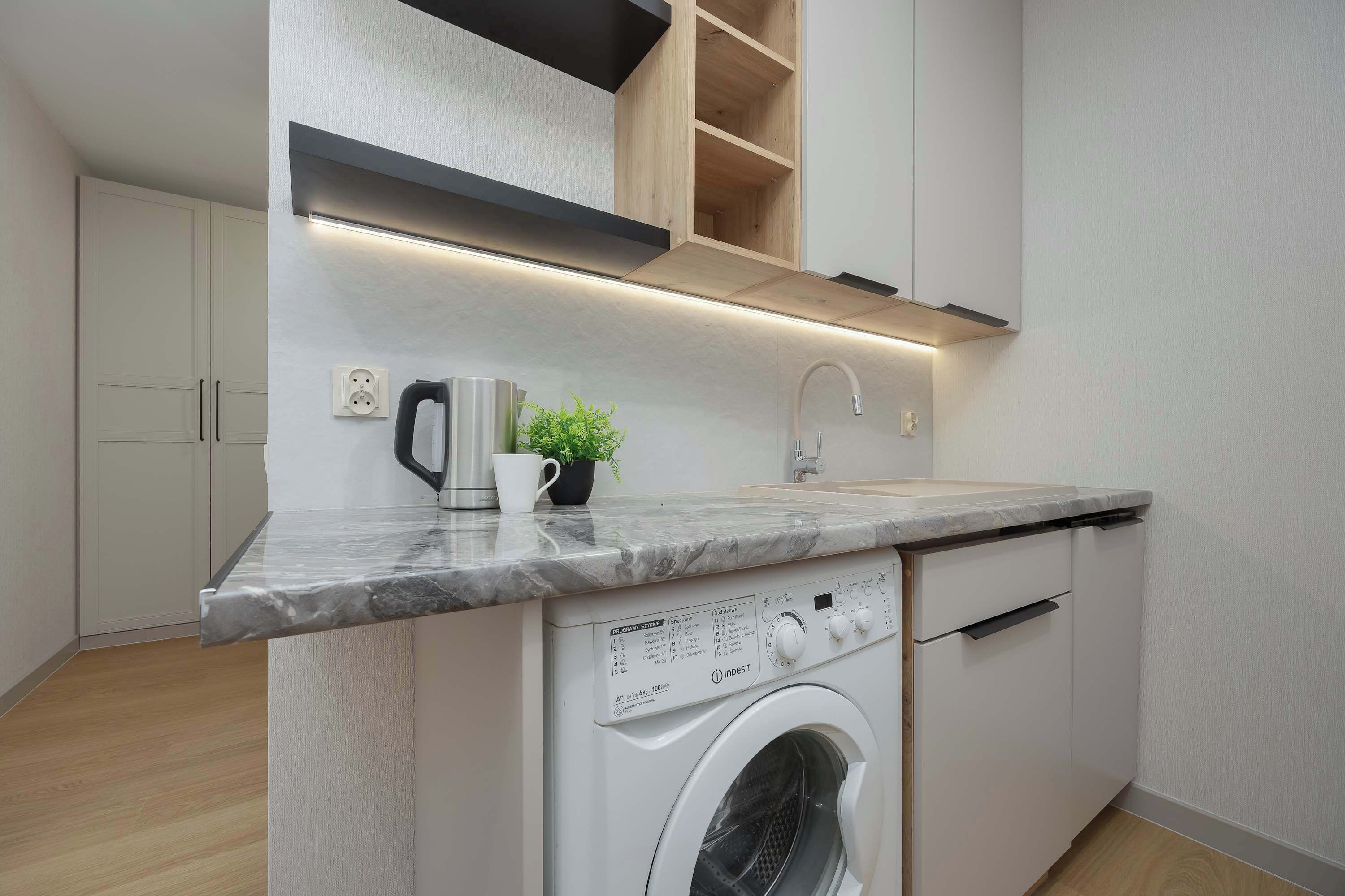 A compact kitchen with a built-in washing machine, a coffee maker, and a small plant on the countertop.