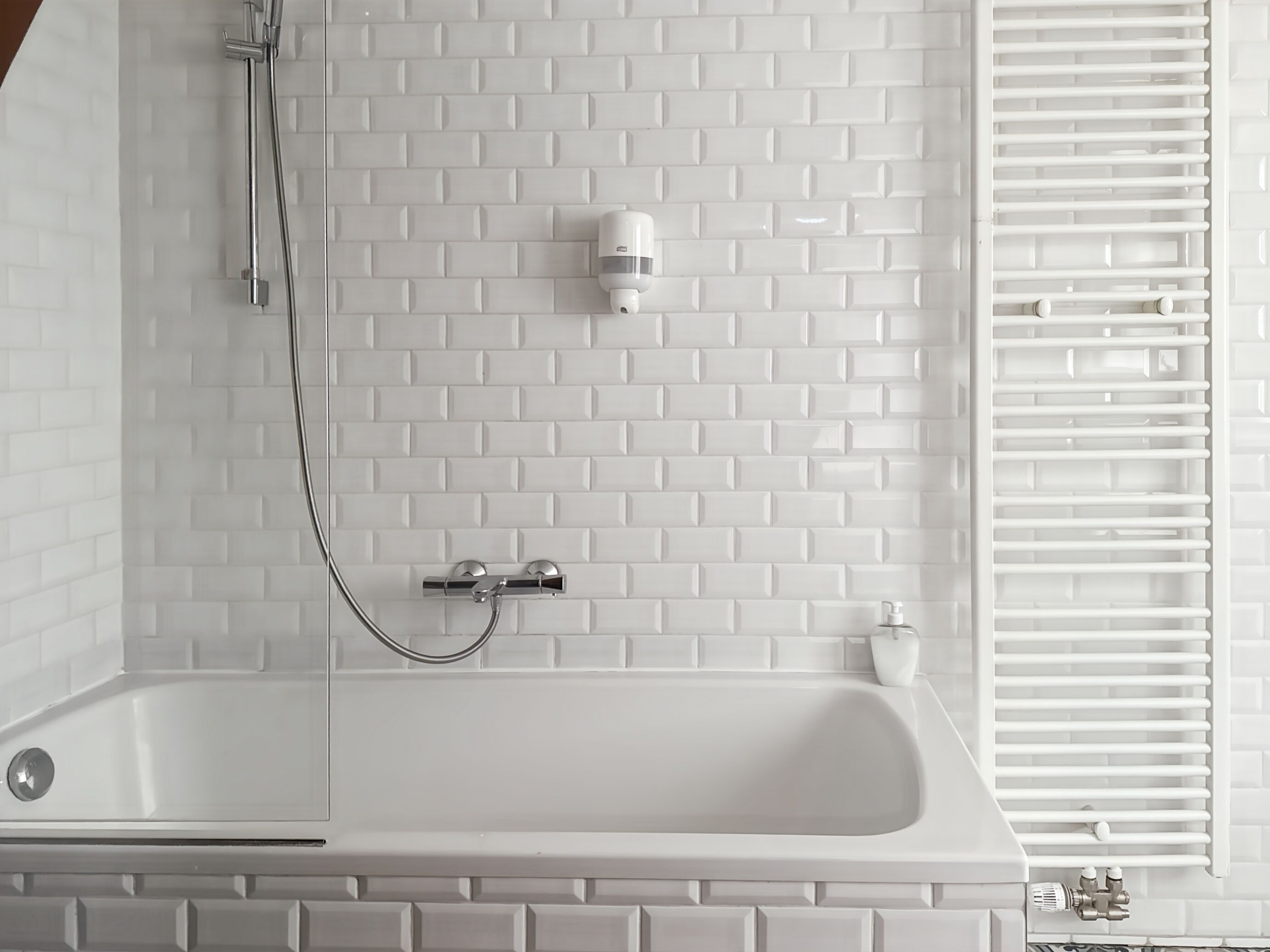 Een badkamer met een witte badkuip, een handdouche, een wandmengkraan en een radiator.