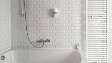 Een badkamer met een witte badkuip, een handdouche, een wandmengkraan en een radiator.