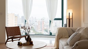 A living room with a view of a cityscape, a round table with a vase and candles, a brown chair, and a beige sofa. - 3-bedroom apartment with high-rise balcony Near Xintiandi CBD200m to  Metro. (Shanghai)