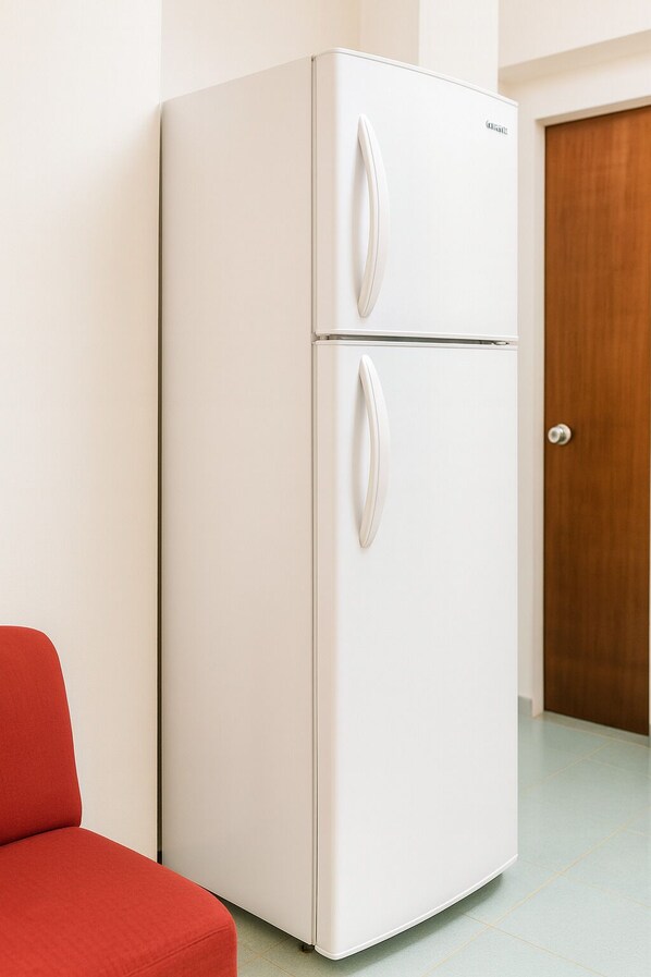 Ein weißer Kühlschrank mit zwei Türen, eine Holztür im Hintergrund und ein roter Stuhl auf der linken Seite.