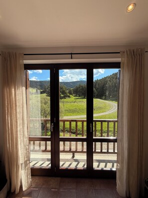 Ein Zimmer mit einer großen Schiebetür, die auf einen Balkon mit Blick auf eine grüne Landschaft und eine Straße führt.