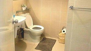 Et badeværelse med toilet, håndvask, spejl og bruseområde.