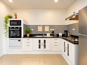 A modern kitchen with white cabinetry, black appliances, and a tiled backsplash. - Luxurious Villa with Private Pool and Stunning Views (ตำบล ฉลอง)