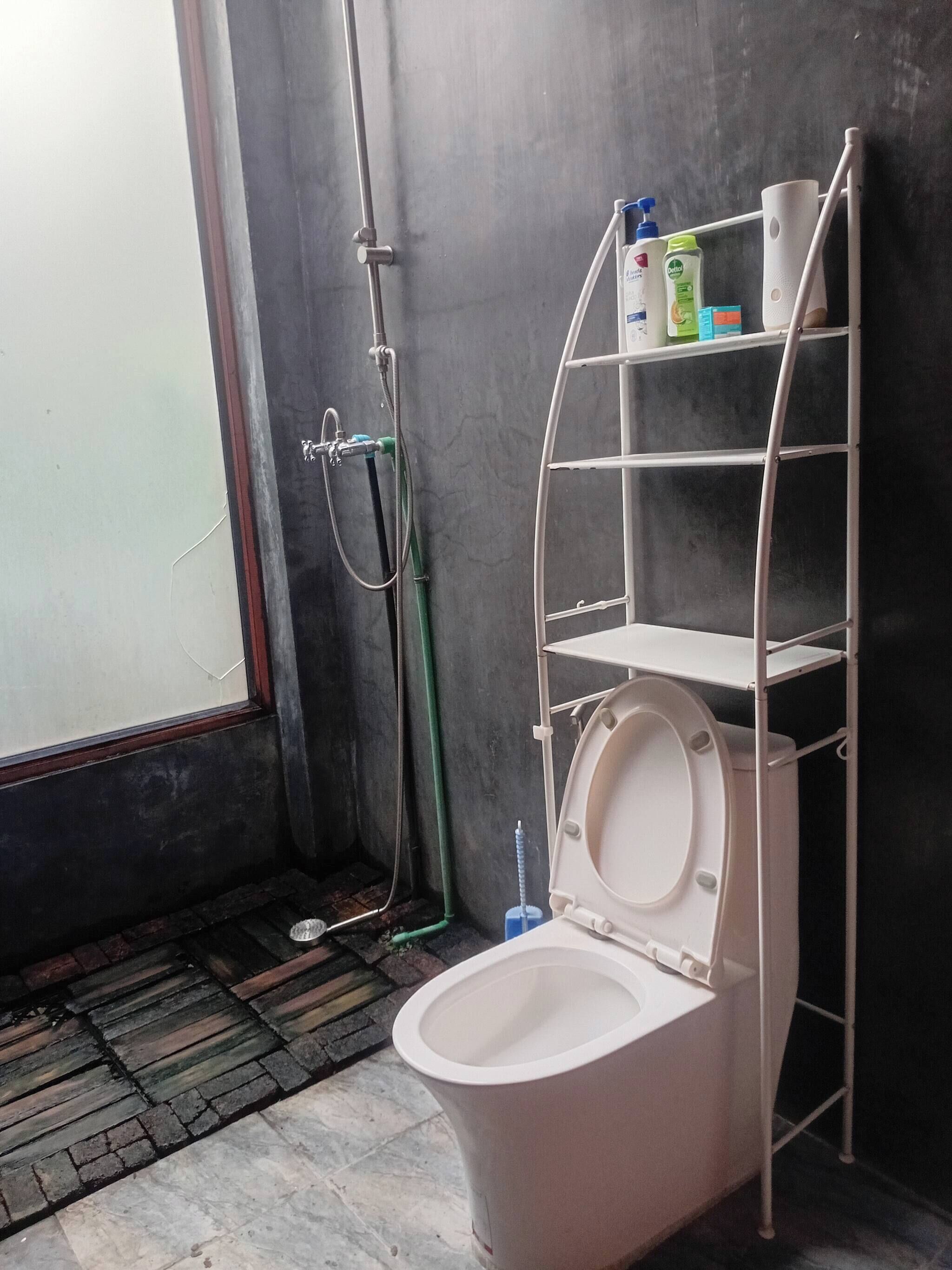 Ein Badezimmer mit Toilette, Dusche, Ablage für Toilettenartikel und einem Fenster.