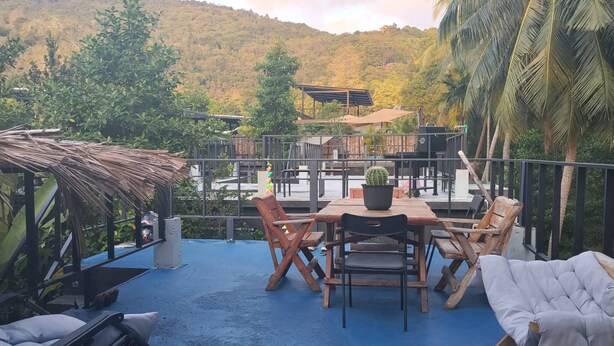 A patio with a table and chairs, a small potted plant, and a thatched roof structure. - Crystal Jungle House - Rooftop mountain view (Ko Pha Ngan)