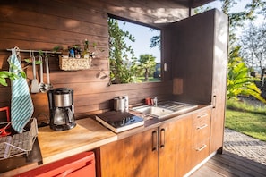 A modern kitchen with wooden cabinetry, a coffee maker, a sink, and a window overlooking greenery. - 'Silves' Cabin-Cato Preto-Adults-Only Guesthouse (Silves)
