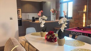 A modern kitchen with dark cabinets and a built-in oven, a dining area with a white table and gold placemats, and a billiards table in the background. - Winter stays, Pool, Wi-Fi, Parking, 3double beds (Bradford)