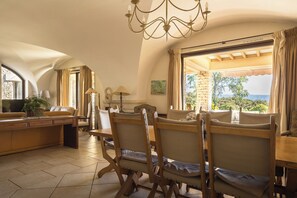 Ein sonnendurchfluteter Essbereich mit Blick ins Freie, ausgestattet mit einer Chandelier, Holzsesseln und einem Tisch.