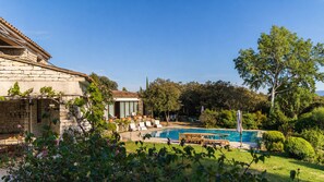 Ein Steinhaus mit Pool, Sitzgelegenheiten im Freien und viel Grün.