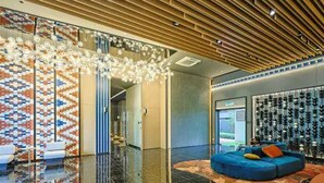 Un hall d’entrée moderne avec un sol réfléchissant, un canapé bleu agrémenté de coussins et un mur à motifs.