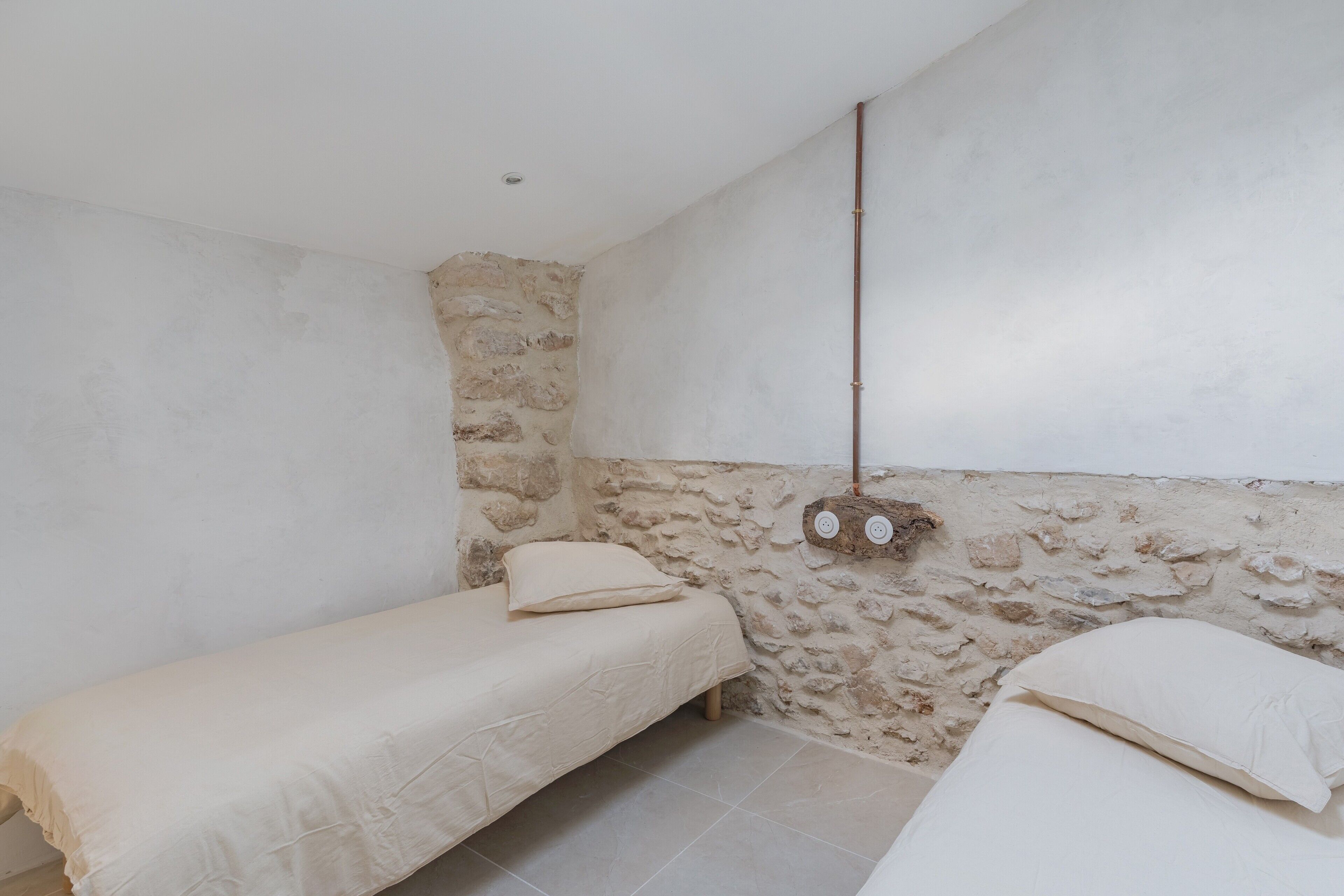 A small, simple room with two beds, a stone wall, and a hanging light fixture.