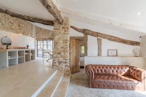 A spacious living area with exposed wooden beams, a stone wall, and a leather sofa.