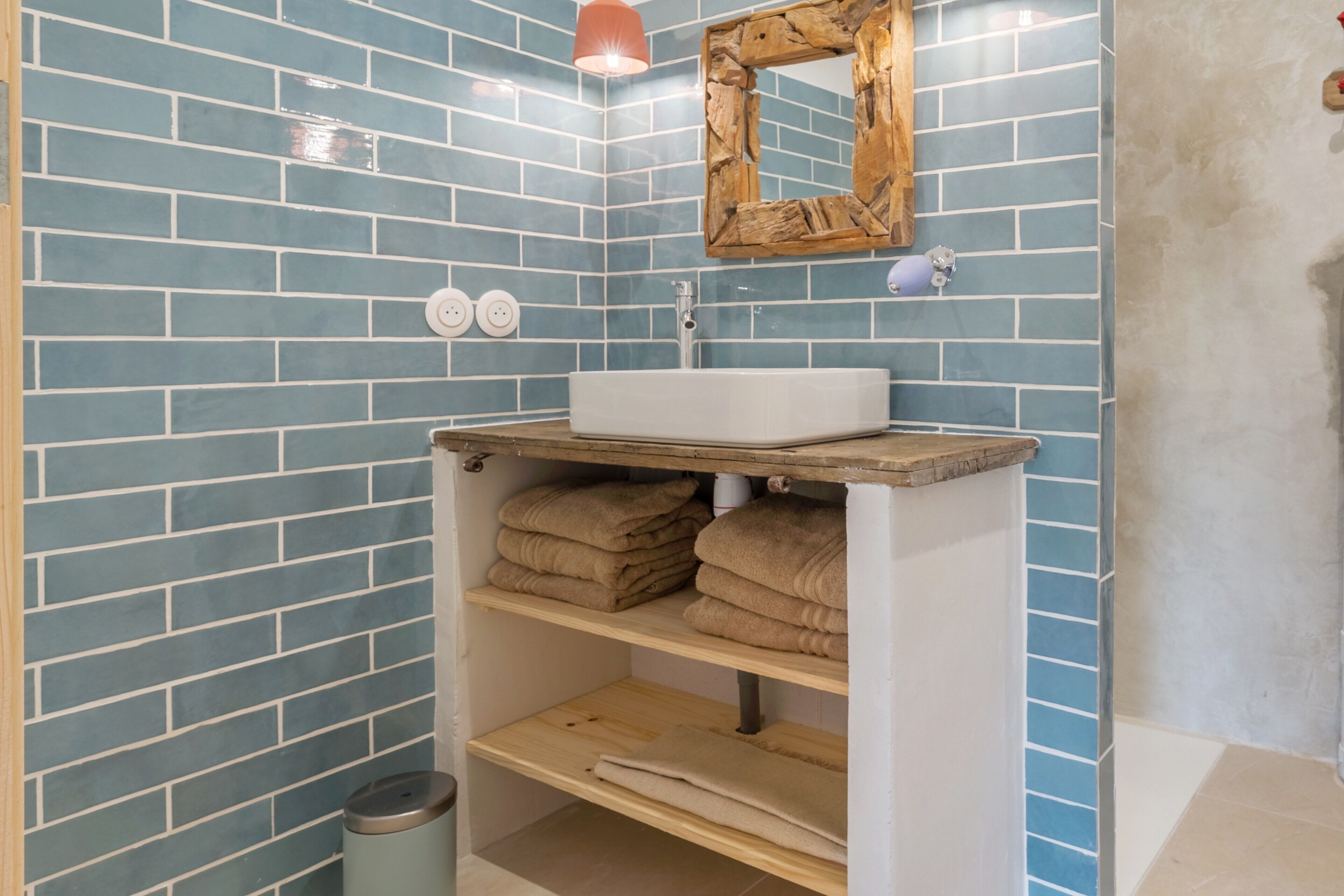 Un bagno con parete in piastrelle blu, un mobile bagno in legno con lavabo e scaffali con asciugamani.