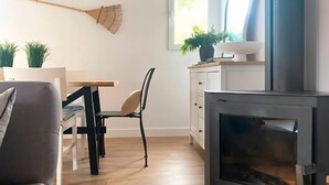 A living room with a sofa, a dining table with chairs, a black TV stand, a fireplace, and a window with plants. - Rural apartment in Cal Rosal, Berga - Air conditioning and nature (Avià)