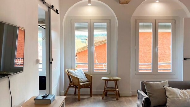 A room with a TV, a chair, a small table, and two windows with a view of a red landscape. - Rural apartment in Cal Rosal, Berga - Air conditioning and nature (Avià)