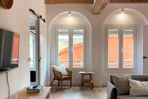 A room with a TV, a chair, a small table, and two windows with a view of a red landscape. - Rural apartment in Cal Rosal, Berga - Air conditioning and nature (Avià)