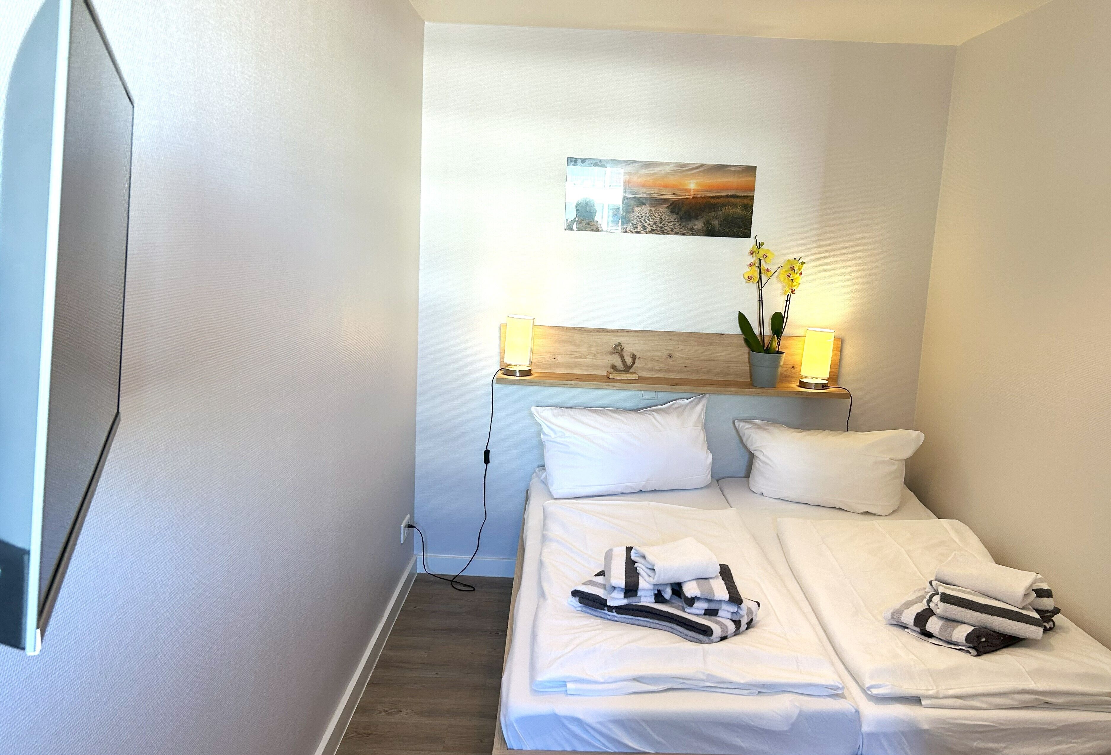 Ein Hotelzimmer mit Bett, weißen Kissen, einem Nachttisch mit Lampe, einem Bild an der Wand und einem Fenster.