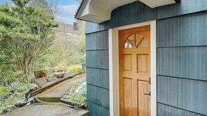 Een houten deur met een ruit, een blauwe buitenmuur en een tuin met planten en een waterslang.