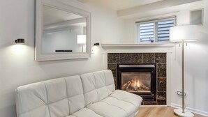 Een woonkamer met een witte bank, een open haard, een spiegel en een vloerlamp.