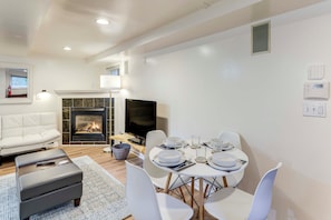 A modern living room with a fireplace, a flat-screen TV, a dining table set for four, and a white sofa. - Walkable Green Lake Studio w/ Fireplace (Seattle)